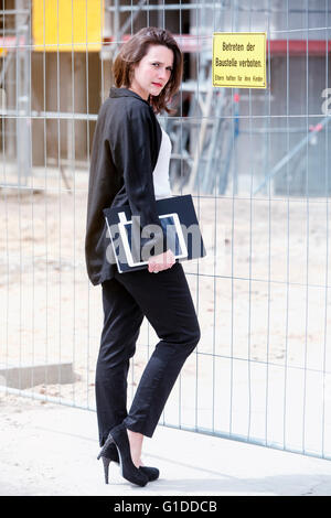 Young woman standing in front of construction site et la tenue de livre à Banque D'Images