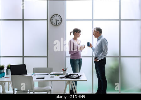 Les employés de bureau gaie dans le bureau, se détendre, avoir une pause-café et discuter ensemble, ils sont debout devant le Banque D'Images