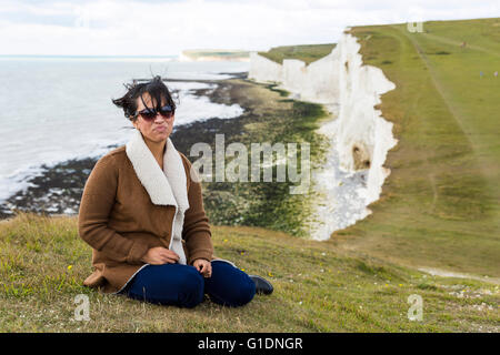 Jeune femme portant des lunettes de soleil assis sur l'herbe. Les sept Sœurs, les falaises du parc national vers le sud, East Sussex, UK Banque D'Images