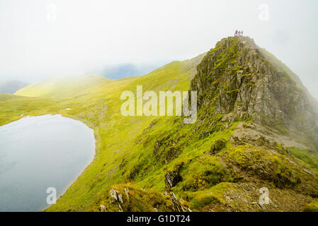 Les randonneurs dans le brouillard sur le bord avançant à Helvellyn dans le Lake District avec Red Tarn ci-dessous Banque D'Images