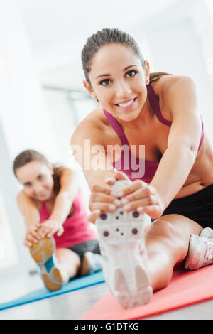 Souriante jeune femme à la salle de sport de faire un exercice d'étirement des jambes sur une natte, concept de santé et de remise en forme Banque D'Images