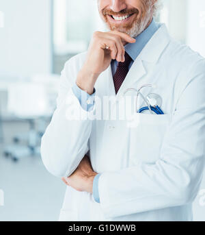 Professional doctor posing at hospital and smiling at camera with hand on chin
