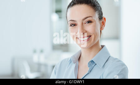 Beau confident business woman posing and smiling at camera, cabinet intérieur sur l'arrière-plan Banque D'Images
