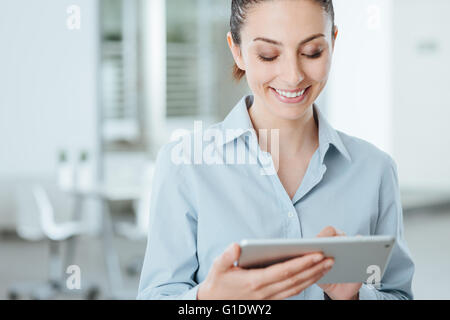 Young smiling business woman en utilisant un écran tactile numérique et utiliser des applications, il est debout dans le bureau Banque D'Images