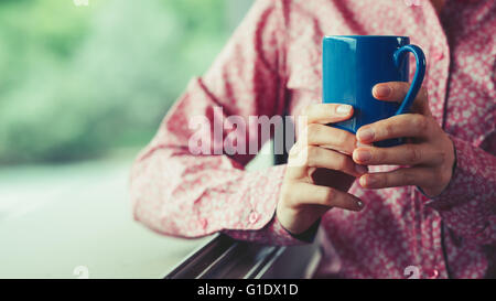 Fenêtre à femme tenant une tasse et d'avoir une pause-café, mains close up Banque D'Images