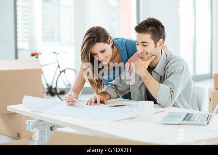 La planification de leur couple Yougn nouvelle maison de rêve, il est assis au bureau et elle s'appuie sur un projet, des boîtes en carton sur l'arrière-plan Banque D'Images