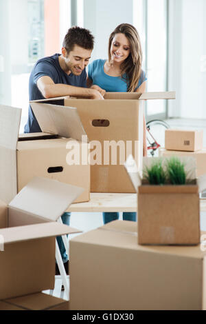 Smiling young couple déballage de cartons dans une nouvelle maison, il est à la recherche d'objets dans une grande boîte sur une table Banque D'Images