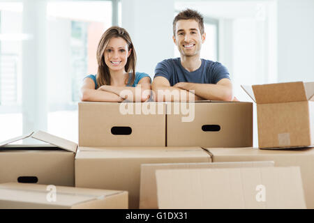 Jeune couple posing with arms crossed appuyée sur des boîtes en carton et smiling at camera, concept à la réinstallation Banque D'Images