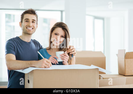 Couple heureux la planification et de la conception de leur nouvelle maison entourée par des boîtes en carton, il s'appuie sur un projet Banque D'Images