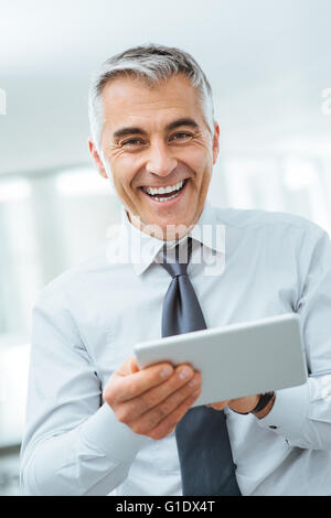 Smiling confident businessman looking at camera et à l'aide d'un écran tactile numérique Banque D'Images