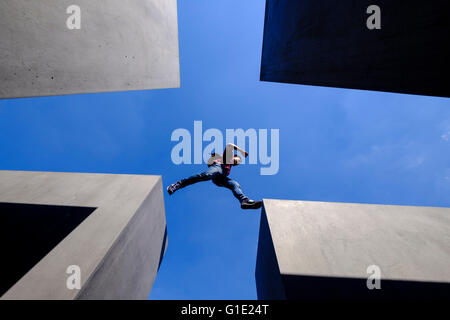 Man jumping entre piliers en béton au Mémorial aux Juifs assassinés d'Europe , Holocaust Memorial, à Berlin, Allemagne Banque D'Images