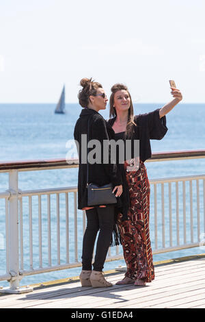 Bournemouth, Dorset, UK 14 mai 2016. Deux jeunes femmes posant pour une sur la jetée de Bournemouth selfies sur une chaude après-midi ensoleillée, avec un yacht de voile au loin. Credit : Carolyn Jenkins/Alamy Live News Banque D'Images