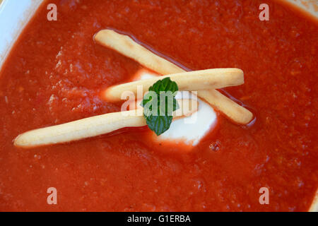 Feuilles de menthe, la crème sure et gressins croustillants délicieux en soupe à la tomate. Banque D'Images