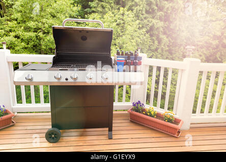 La lumière du jour tombant sur open grande cuisinière barbecue, bière en bouteille, coupe, et sur la caisse de bois de cèdre avec arbres en arrière-plan. Banque D'Images