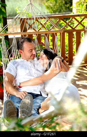 Portrait jeune couple vêtu de blanc sur un hamac de corde sur la terrasse d'une maison de campagne d'amour à la vue arrière Banque D'Images