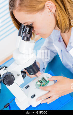 Parution du modèle. À l'aide de technicienne d'examiner au microscope de circuit imprimé. Banque D'Images