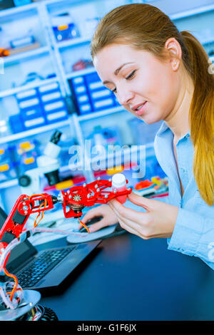 Parution du modèle. Jeune femme travaillant sur un bras robotique. Banque D'Images