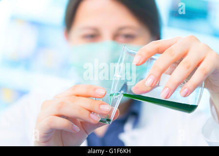 Parution du modèle. Female chemist un liquide vert dans une tasse en plastique. Banque D'Images