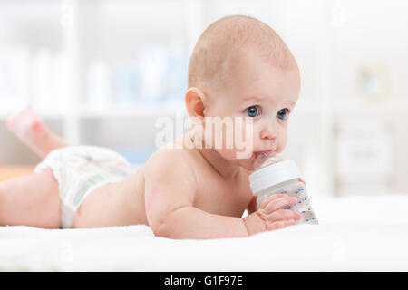 Bébé bébé boit de l'eau de la bouteille couchée sur le lit. Portée de l'enfant érythème dans la salle de séjour. Banque D'Images