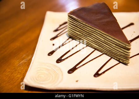 Gâteau de crêpe dans un plat carré de style japonais sur la table en bois avec une sauce au chocolat en zigzag. Banque D'Images