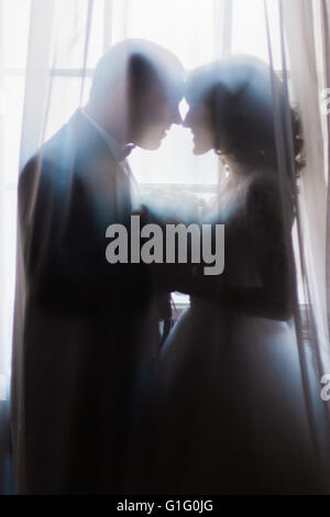 Silhouette de la jeune mariée et se toilettent embrassant holding bouquet contre la fenêtre avec des rideaux Banque D'Images