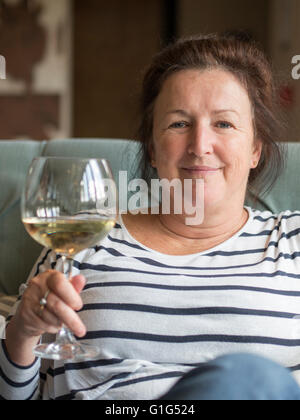 A middle-aged woman holding d'un grand verre de vin blanc. Banque D'Images
