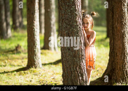 10-year-old girl regarde de derrière un arbre. Banque D'Images