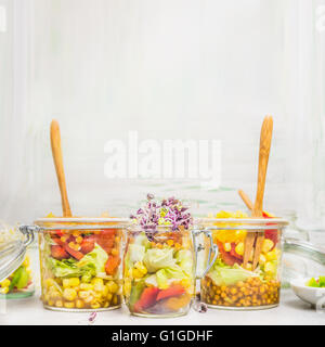 De délicieuses salades dans des bocaux en verre avec des légumes, des lentilles, du maïs et des germes de lumière sur fond de bois, vue de côté, la place pour le texte. Banque D'Images