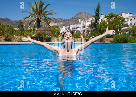 Locations de brunette smiling woman with white bikini à bras tendus et de gestes ou de la victoire d'accueil dans l'eau bleu o Banque D'Images