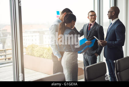 L'équipe d'affaires multiethniques, debout devant une fenêtre dans une salle de conférence de l'office d'avoir une discussion, sun flare et co Banque D'Images