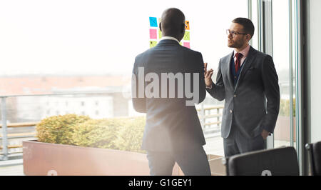 Deux cadres d'affaires élégant mâle multiracial dans une discussion animée en face d'une fenêtre lumineuse avec des reflets et copy space Banque D'Images