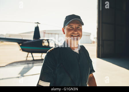Portrait of male pilot in airplane hangar avec un hélicoptère en arrière-plan Banque D'Images