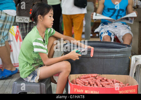 Une jeune fille Philippine saucisses coupes dans le marché du carbone situé au centre-ville de Cebu City, Philippines Banque D'Images