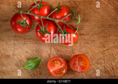 Tomates cerises coupées en deux avec feuille de basilic sur table en bois Banque D'Images