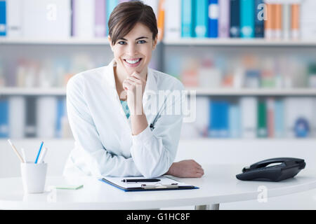 Attractive young woman leaning on la clinique/24 with hand on chin, il est smiling at camera, un personnel médical Banque D'Images