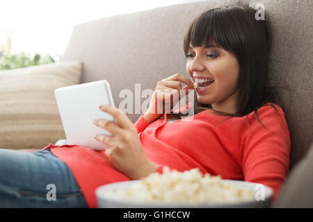 Jolie femme détente sur le canapé à la maison, c'est de regarder des vidéos en ligne et eating popcorn, streaming films concept Banque D'Images