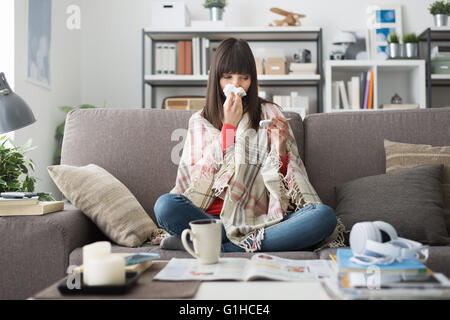 Femme malade avec le rhume et la grippe, elle se repose sur le canapé à la maison et la mesure de la température du corps avec un thermomètre Banque D'Images