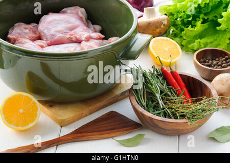 Les viandes de lapin aux légumes et herbes dans un pot en céramique ronde sur la surface de la table en bois blanc Banque D'Images