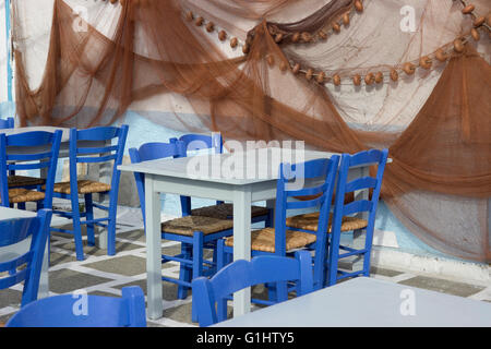 Chaises bleu, cyan vide du the tables sur sol à damiers et les filets de pêche accroché à la décoration murale.Myrina Limnos, Grèce. Banque D'Images