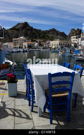 Restaurant table avec sièges bleu, décoré de Pélargonium pot de fleurs, donnant sur le château et l'architecture de la ville. Limnos Banque D'Images