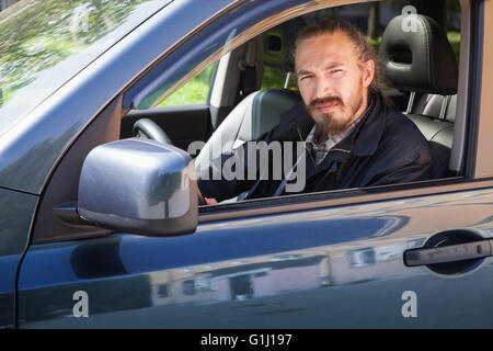 Sérieux barbu Asian man avec clés en tant que conducteur de suv japonais moderne, extérieur portrait dans la fenêtre de la voiture ouverte Banque D'Images