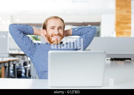 Cheerful young businessman détendue avec laptop sitting on travail avec les mains derrière la tête Banque D'Images
