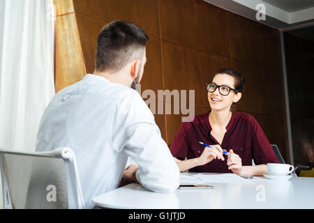 Smiling beautiful young woman lunettes parler aux jeunes dans la salle de réunion Banque D'Images