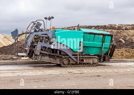 Vue latérale sur la machine de pose d'asphalte au chantier de construction. L'asphalte chaud se répand avec machine à paver sur sol préparé. Banque D'Images