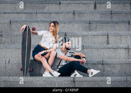 Jeune couple élégant escalier en béton sur avec un longboard Banque D'Images