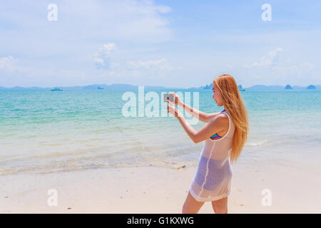 Heureux belle blonde en bikini en tenant une auto photo sur une belle plage ensoleillée Banque D'Images