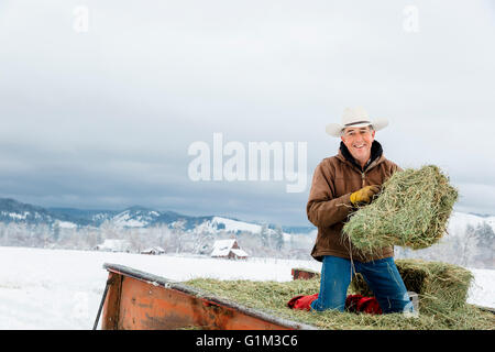 Caucasian farmer hauling hay in snowy field Banque D'Images