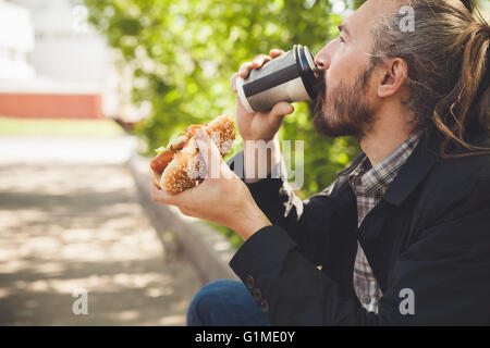 Homme asiatique barbus boire du café avec hot dog en été Parc, piscine en plein air avec portrait de profil selective focus Banque D'Images