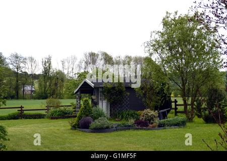 Abris de jardin en bois à son tour plus sombres dans une pelouse avec un parterre de fleurs. Banque D'Images