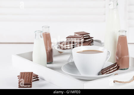 Tasse de café et quelques bouteilles de lait et chocolat lait frappé sur un plateau blanc sur fond blanc volets Banque D'Images